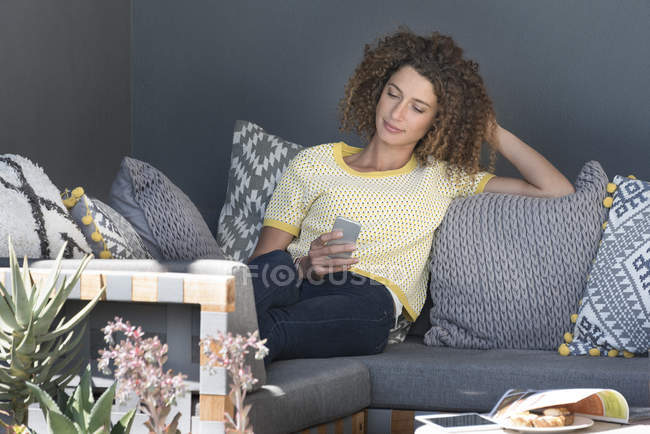Frau sitzt zu Hause auf Couch und nutzt Smartphone — Stockfoto