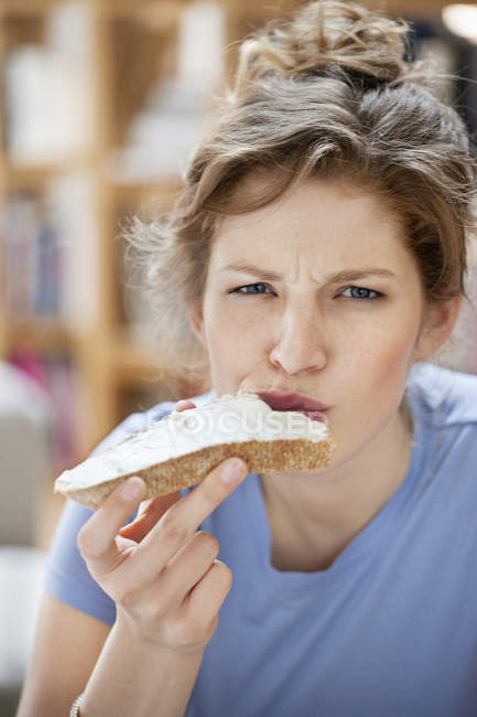 Porträt einer grimmigen Frau, die Toast mit Sahneaufstrich isst — Stockfoto