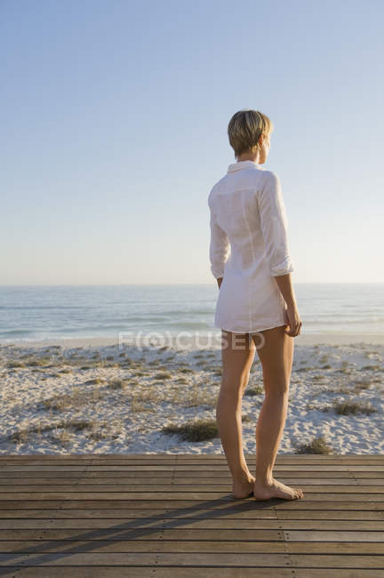 Woman with short hair standing on boardwalk on sea coast and looking at view — Stock Photo