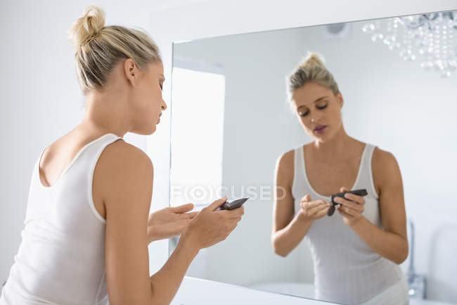 Blonde jeune femme appliquant hydratant sur le visage dans la salle de bain — Photo de stock