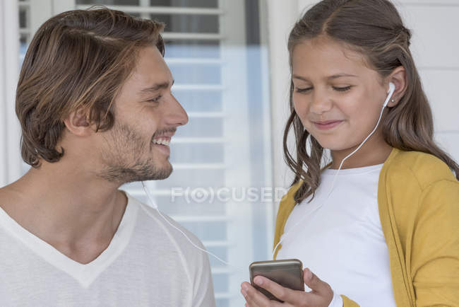 Padre feliz con hija pequeña escuchando música en el teléfono móvil con auriculares - foto de stock