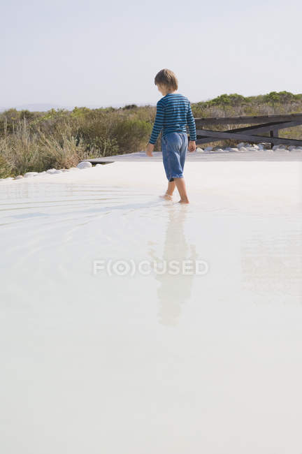 Visão traseira do menino caminhando na piscina infinita — Fotografia de Stock