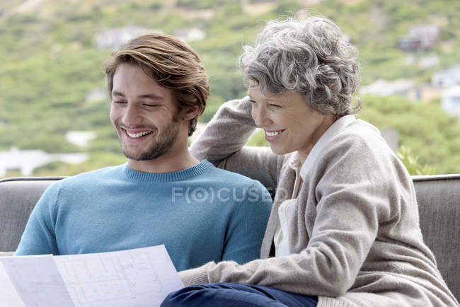 Happy mother with adult son reading blueprint outdoors — Stock Photo