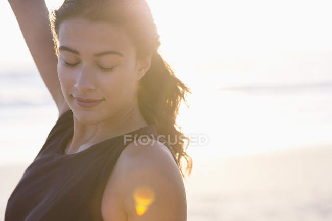 Sorridente giovane donna in piedi sulla spiaggia alla luce del sole — Foto stock