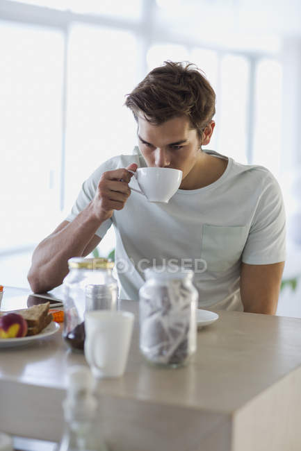 Крупный план молодого человека, пьющего кофе дома — стоковое фото