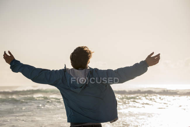 Felice giovane uomo con le braccia distese in piedi sulla spiaggia — Foto stock