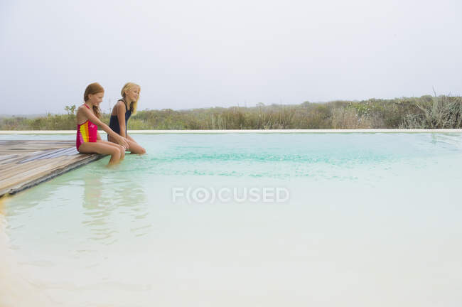 Duas garotas sentadas em uma plataforma em uma piscina infinita — Fotografia de Stock