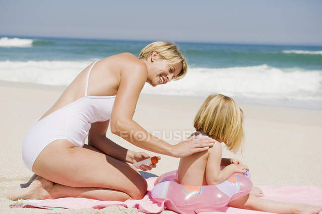 Frau trägt Sonnencreme auf Tochter am Sandstrand auf — Stockfoto