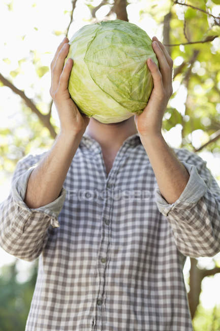 Man holding cabbage in front of face in garden — Stock Photo