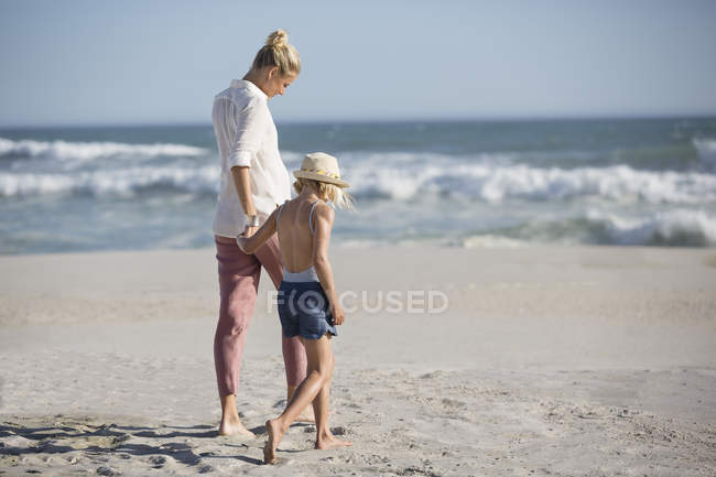 Femme blonde et fille marchant sur la plage de sable — Photo de stock