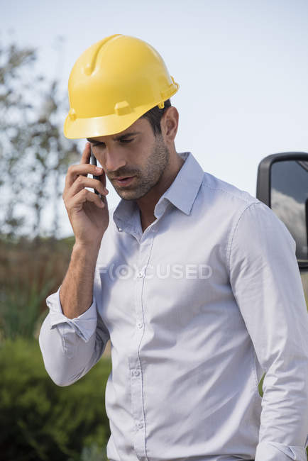 Male engineer in helmet talking on mobile phone outdoors — Stock Photo