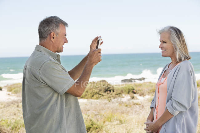 Mann fotografiert Ehefrau mit Handy am Strand — Stockfoto