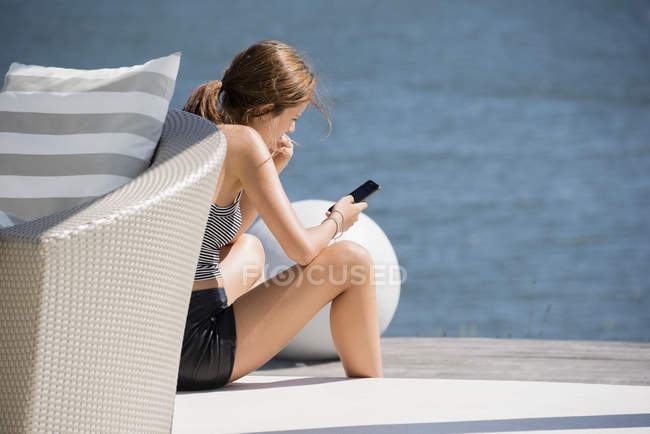 Young woman using smartphone on lake shore — Stock Photo