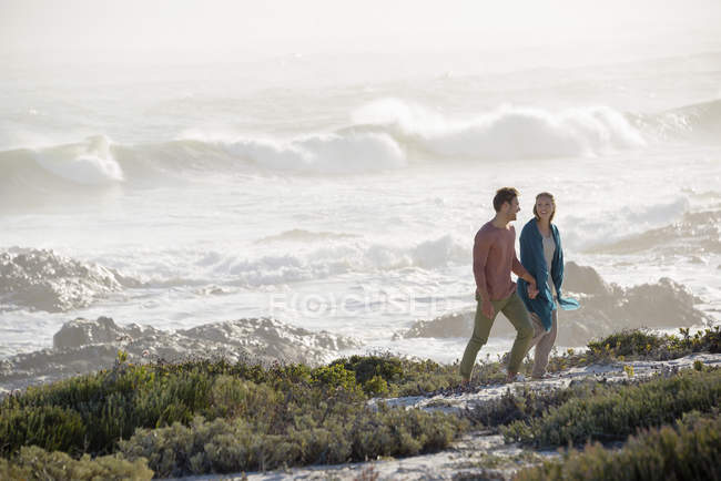 Casal relaxado andando na costa com vegetação — Fotografia de Stock
