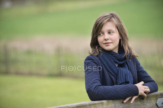 Thoughtful teenage girl looking away near wooden fence in park on blurred background — Stock Photo