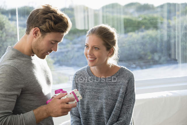 Woman looking at man with birthday gift in front of window pane — Stock Photo