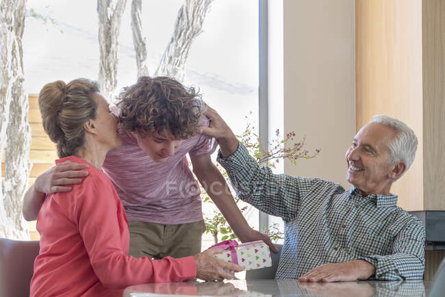 Avós felizes e neto adolescente com presente de aniversário em casa — Fotografia de Stock