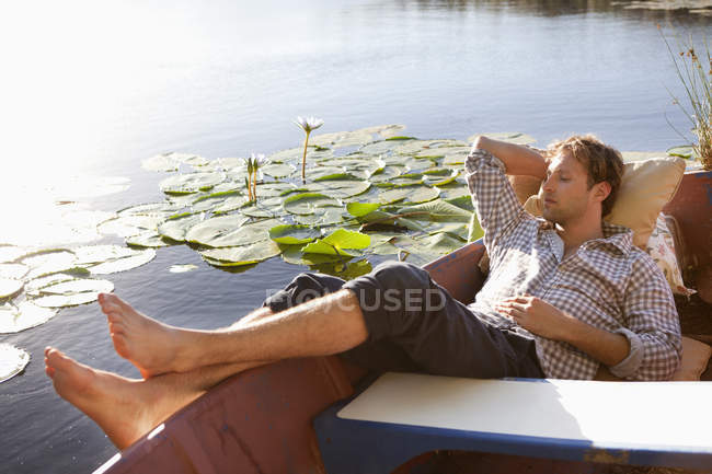 Розслаблений молодий чоловік спить у човні на озері в сільській місцевості — стокове фото