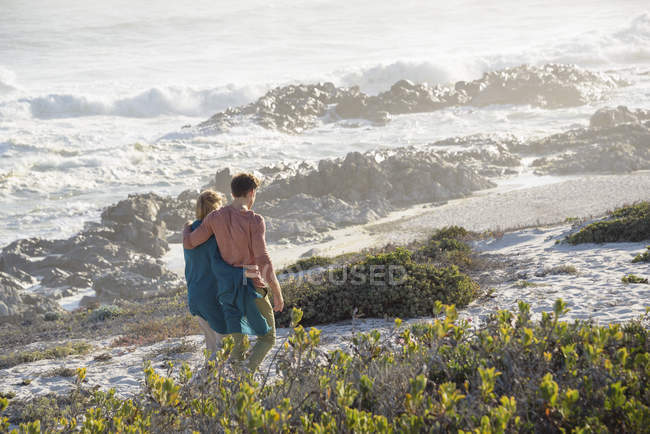 Pareja romántica caminando por la costa con vegetación a la luz del sol - foto de stock