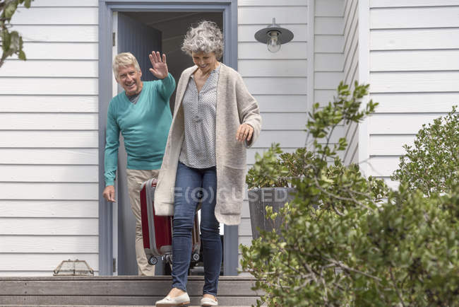 Glücklicher Senior winkt Frau mit Koffer im Treppenhaus zu — Stockfoto
