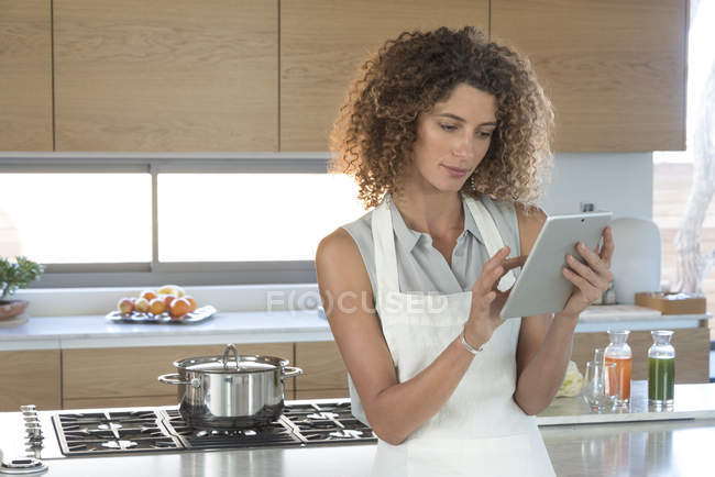 Mulher em avental usando tablet digital na cozinha — Fotografia de Stock