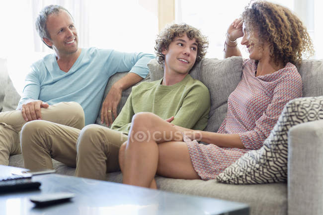 Família feliz sentada no sofá e conversando na sala de estar em casa — Fotografia de Stock