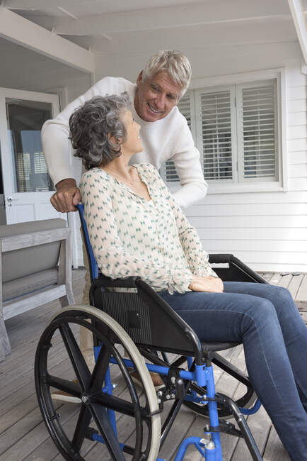 Uomo anziano che parla con sua moglie in sedia a rotelle sul portico — Foto stock