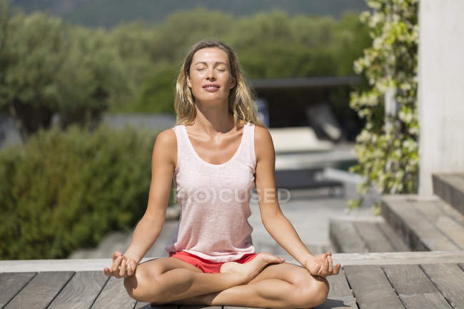 Розслаблена жінка робить йогу на дерев'яній терасі в природі — стокове фото