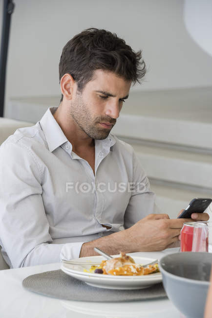Nachdenklicher Mann nutzt Smartphone am Esstisch — Stockfoto