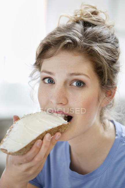 Portrait of young woman eating toast with cream spread — Stock Photo