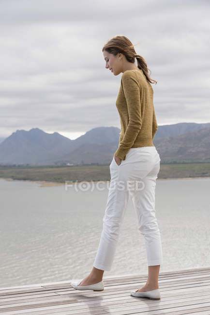 Young woman standing on deck at lake shore — Stock Photo