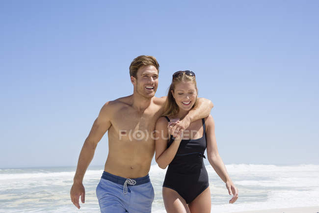 Coppia felice in costume da bagno a piedi sulla spiaggia sotto il cielo blu — Foto stock