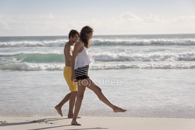 Verspieltes junges Paar spaziert gemeinsam am Strand — Stockfoto