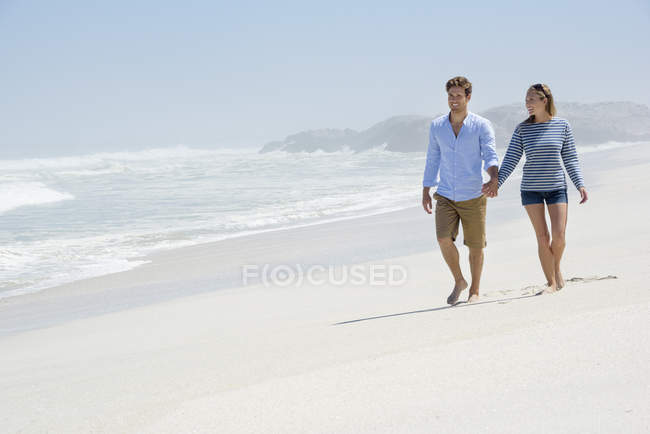 Счастливая пара, идущая по песчаному пляжу держась за руки — стоковое фото