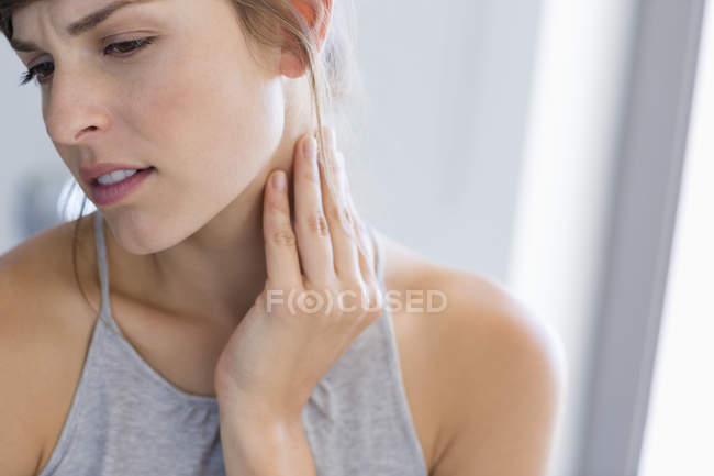 Close-up of young woman massaging neck on grey background — Stock Photo