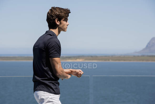 Молодий чоловік стоїть на балконі на відкритому повітрі з видом на море — стокове фото