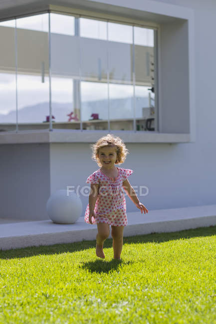 Милая малышка гуляет по зеленой лужайке летом на открытом воздухе — стоковое фото