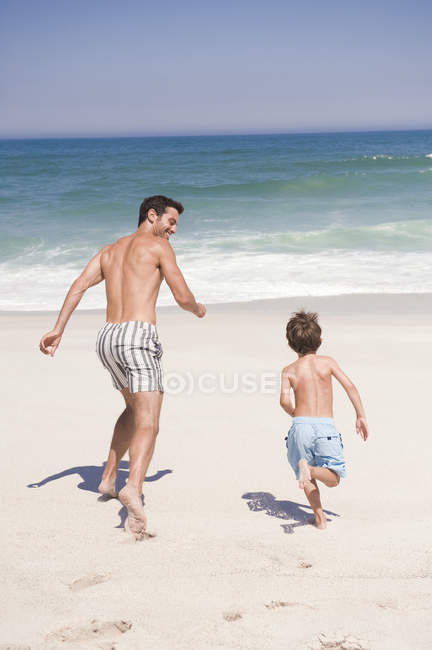 Hombre corriendo con su hijo en la playa de arena - foto de stock