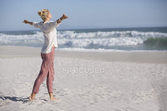 Розслаблена молода жінка з простягнутою рукою стоїть на сонячному пляжі — стокове фото