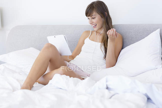 Junge glückliche Frau schaut Film auf digitalem Tablet im Bett — Stockfoto