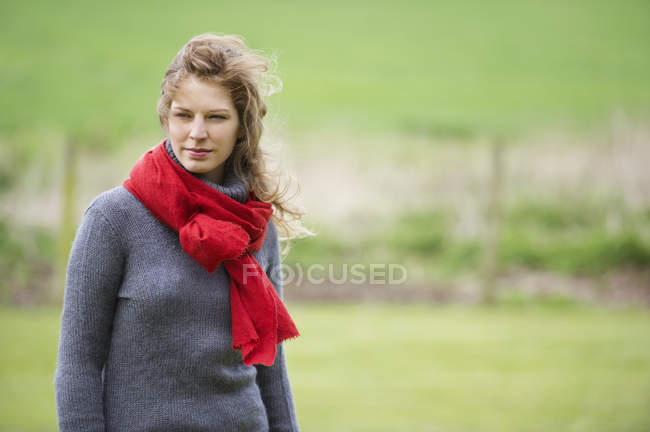 Mujer joven con bufanda roja caminando en el campo - foto de stock