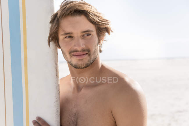 Joyeux jeune homme tenant une planche de surf sur la plage — Photo de stock