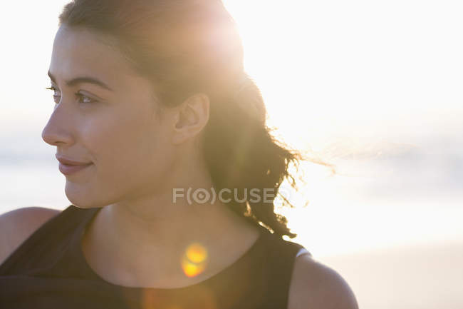 Вдумлива молода жінка стоїть на пляжі на сонячному світлі — стокове фото