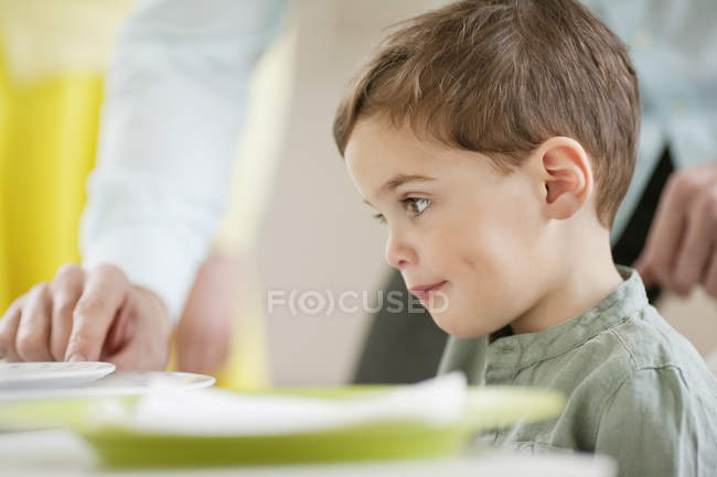 Pequeño niño pensativo sentado en la mesa de comedor - foto de stock