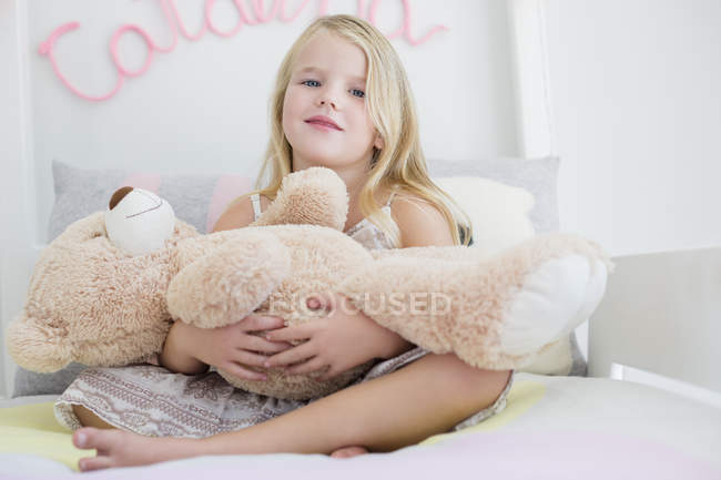 Ritratto di bambina carina che tiene orsacchiotto sul letto — Foto stock