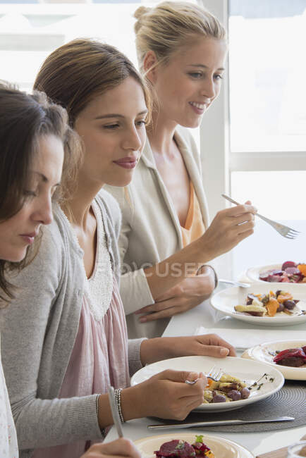 Three beautiful women having lunch at dining table — Stock Photo