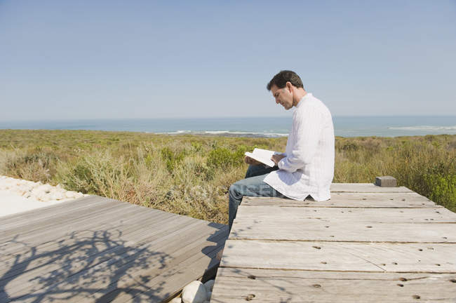 Mann sitzt auf Promenade in der Natur und liest ein Buch — Stockfoto