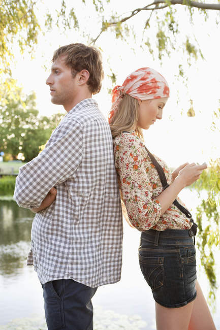 Side view of couple standing back to back with mobile phone — Stock Photo