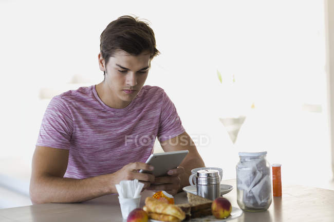 Joven usando tableta digital en la mesa de la cocina - foto de stock