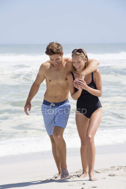 Laughing couple in swimwear walking on sandy beach — Stock Photo